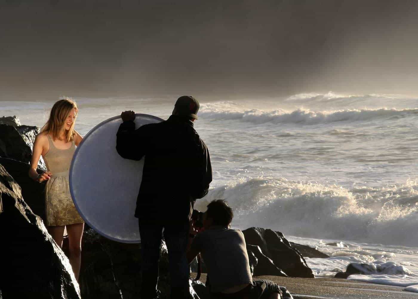 A photographer using a reflector to bounce light onto a model on a beach